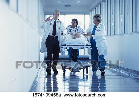 Doctors and a nurse pushing a patient through the hospital corridor on a gurney View Large Photo Image Stock Image - Doctors and a nurse pushing a patient through the hospital corridor on a gurney. Fotosearch