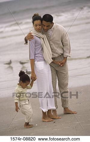 Stock Image - Father and mother walking with their daughter on the beach. Fotosearch