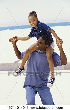 Stock Image - Father carrying his daughter on the beach. Fotosearch