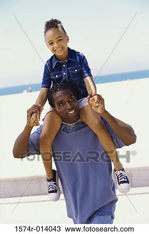 Stock Image - Father carrying his daughter on the beach. Fotosearch