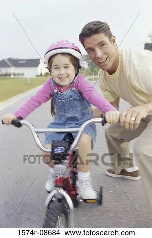 Father helping his daughter ride a bicycle View Large Photo Image Picture - Father helping his daughter ride a bicycle. Fotosearch