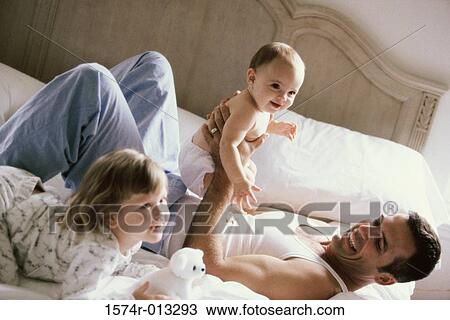Stock Image - Father playing with his son and daughter on a bed. Fotosearch
