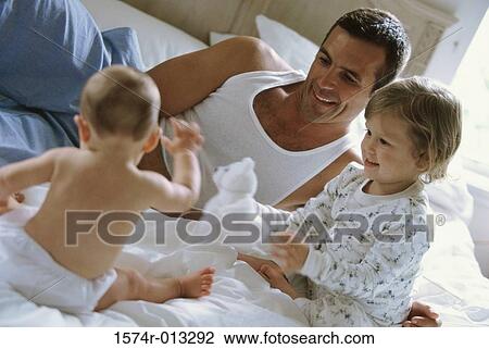 Father sitting with his son and daughter on a bed View Large Photo Image Stock Image - Father sitting with his son and daughter on a bed. Fotosearch