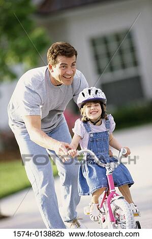 Stock Image - Father teaching his daughter to ride a bicycle. Fotosearch