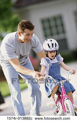 Stock Image - Father teaching his daughter to ride a bicycle. Fotosearch
