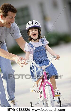 Stock Image - Father teaching his daughter to ride a bicycle. Fotosearch