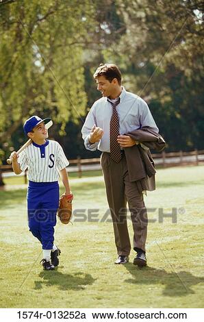 Stock Image - Father walking in the park with his son carrying a baseball bat. Fotosearch