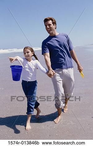 Stock Image - Father walking with his daughter on the beach. Fotosearch