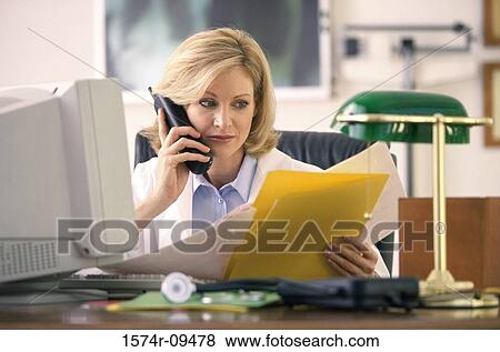 Stock Photo - Female doctor sitting behind a desk talking on a telephone. Fotosearch