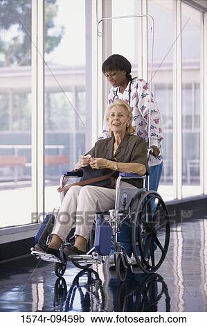 Stock Image - Female nurse pushing a female patient in a wheelchair. Fotosearch
