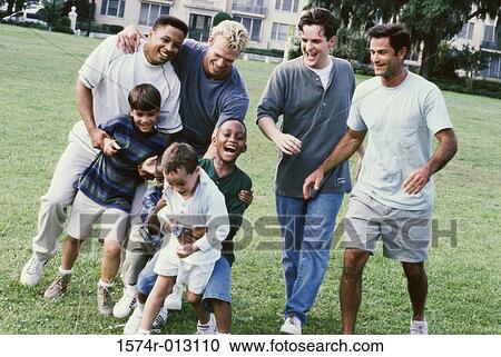 Stock Image - Four fathers with their sons playing in a park. Fotosearch