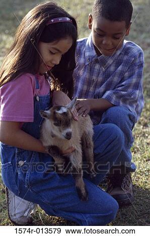 Stock Photo - Girl holding a kid goat in her arms with a boy sitting beside her. Fotosearch