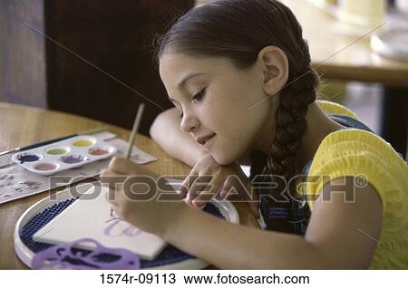 Stock Image - Girl seated at a table painting. Fotosearch