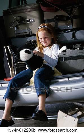 Stock Image - Girl sitting in the back of a car and holding a teddy bear. Fotosearch