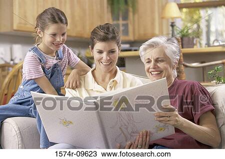 Stock Image - Girl with her mother and grandmother looking at a photo album. Fotosearch