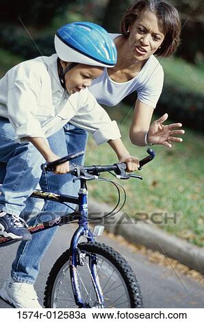 Stock Image - Grandmother teaching her grandson to ride a bicycle. Fotosearch