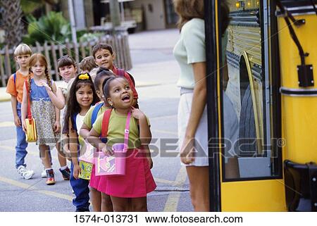 Stock Image - Group of students standing in a row near a school bus. Fotosearch