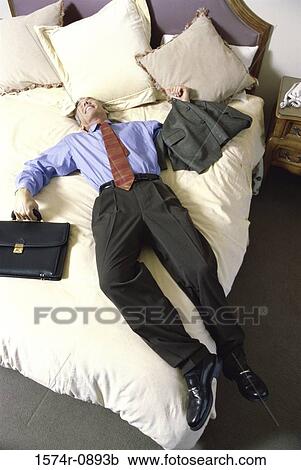 Stock Image - High angle view of a businessman lying on a bed in a hotel room. Fotosearch