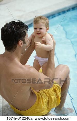 Stock Image - High angle view of a father sitting at the poolside playing with his son. Fotosearch