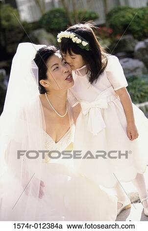 Stock Image - High angle view of a flower girl kissing a bride's cheek. Fotosearch