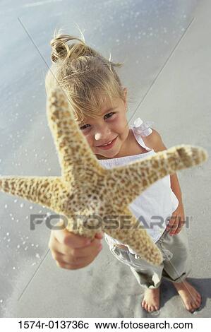High angle view of a girl showing a starfish on the beach View Large Photo Image Stock Image - High angle view of a girl showing a starfish on the beach. Fotosearch