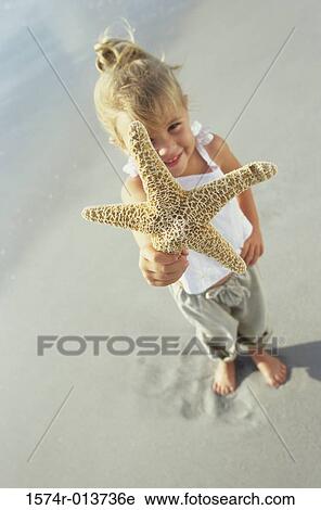 Stock Image - High angle view of a girl showing a starfish on the beach. Fotosearch