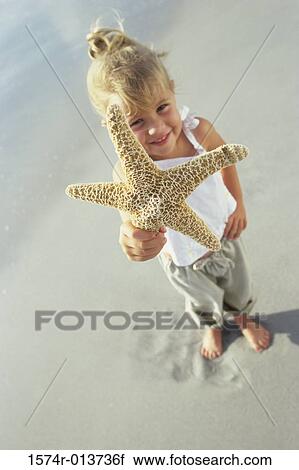 Stock Image - High angle view of a girl showing a starfish on the beach. Fotosearch