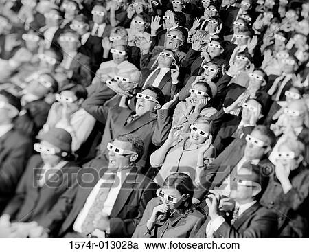 Stock Image - High angle view of a group of spectators sitting in a movie theater wearing 3-D glasses. Fotosearch