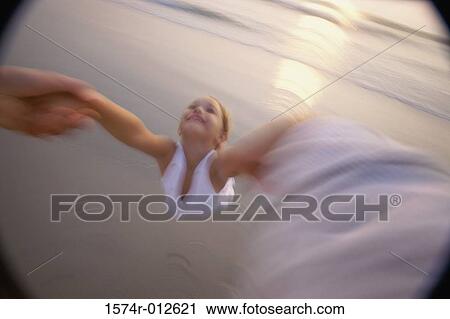 Stock Image - High angle view of a person's hands swinging a girl on the beach. Fotosearch
