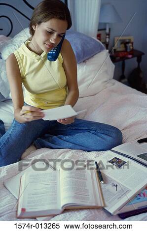 Stock Photography - High angle view of a teenage girl sitting on a bed talking on a cordless phone. Fotosearch
