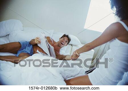 Stock Image - High angle view of a young woman pulling a young man in a bed. Fotosearch