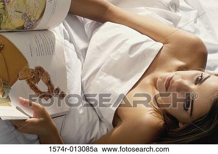 Stock Image - High angle view of a young woman holding a book in bed. Fotosearch
