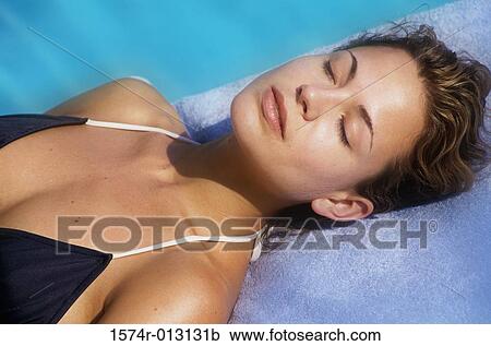 Stock Image - High angle view of a young woman sleeping at poolside. Fotosearch
