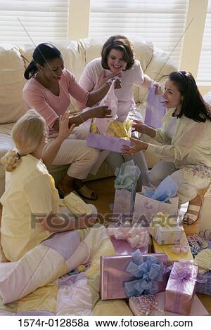 Stock Image - High angle view of four young women unwrapping gifts at a baby shower. Fotosearch