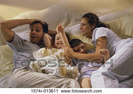 Stock Image - High angle view of parents and their two children playing in bed. Fotosearch