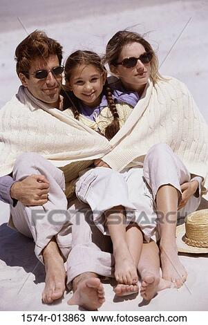 Stock Image - High angle view of parents and their daughter sitting on the beach. Fotosearch