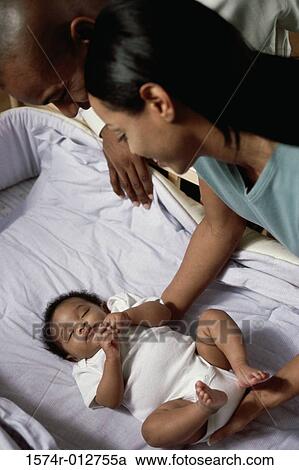 Stock Image - High angle view of parents looking at their baby boy sleeping in a crib. Fotosearch