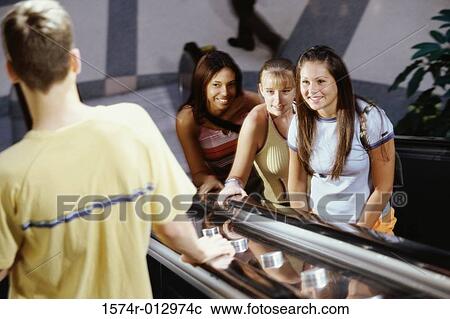 Stock Image - High angle view of three teenage girls and a teenage boy standing on an escalator. Fotosearch