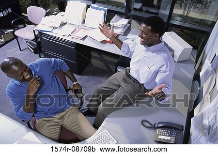 Stock Image - High angle view of two businessmen talking in an office. Fotosearch