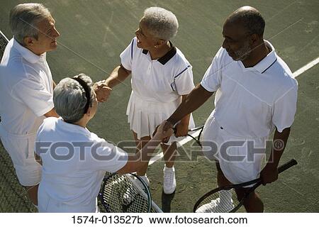 Stock Image - High angle view of two senior couples shaking hands on a tennis court. Fotosearch