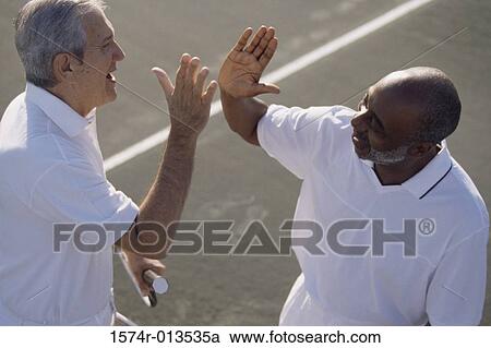 Stock Image - High angle view of two senior men congratulating each other on a tennis court. Fotosearch