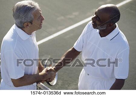 Stock Image - High angle view of two senior men shaking hands on a tennis court. Fotosearch