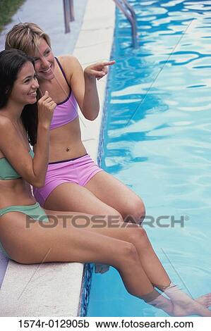 Stock Image - High angle view of two teenage girls sitting at poolside. Fotosearch