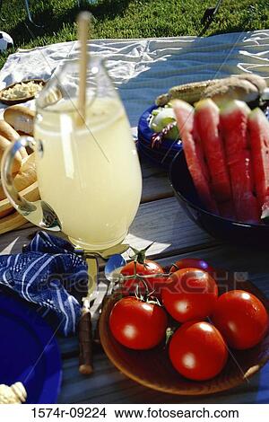 Jug of lemonade with plates of fruit on a picnic table View Large Photo Image Picture - Jug of lemonade with plates of fruit on a picnic table. Fotosearch