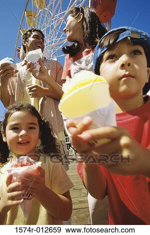 Stock Photo - Low angle view of a brother and sister holding ice cream cones with their parents standing behind them. Fotosearch