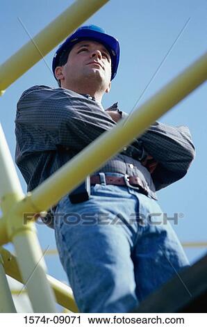Stock Image - Low angle view of a construction worker standing with arms folded. Fotosearch