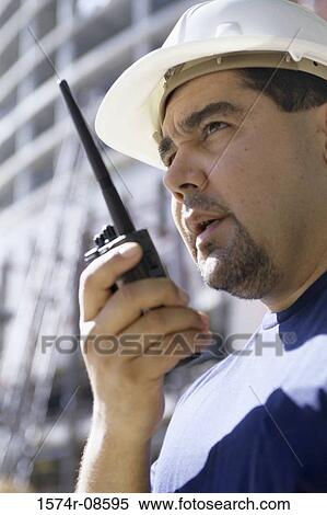 Low angle view of a foreman standing at a construction site talking on a walkie-talkie View Large Photo Image Stock Photography - Low angle view of a foreman standing at a construction site talking on a walkie-talkie. Fotosearch