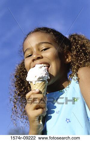 Stock Image - Low angle view of a girl eating an ice cream. Fotosearch