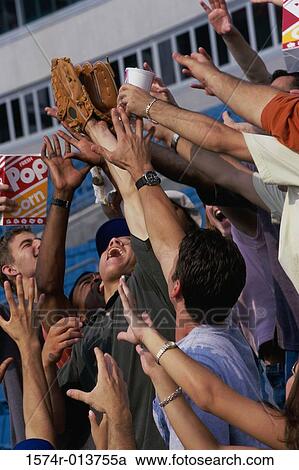 Stock Image - Low angle view of a group of men reaching out for a baseball glove. Fotosearch