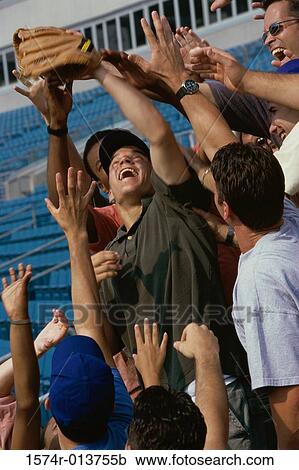 Stock Image - Low angle view of a group of spectators reaching out for a baseball in a stadium. Fotosearch